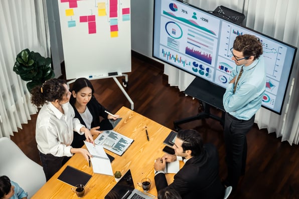 Wide top view of diverse group of business analyst team analyzing financial data report paper on meeting table. 